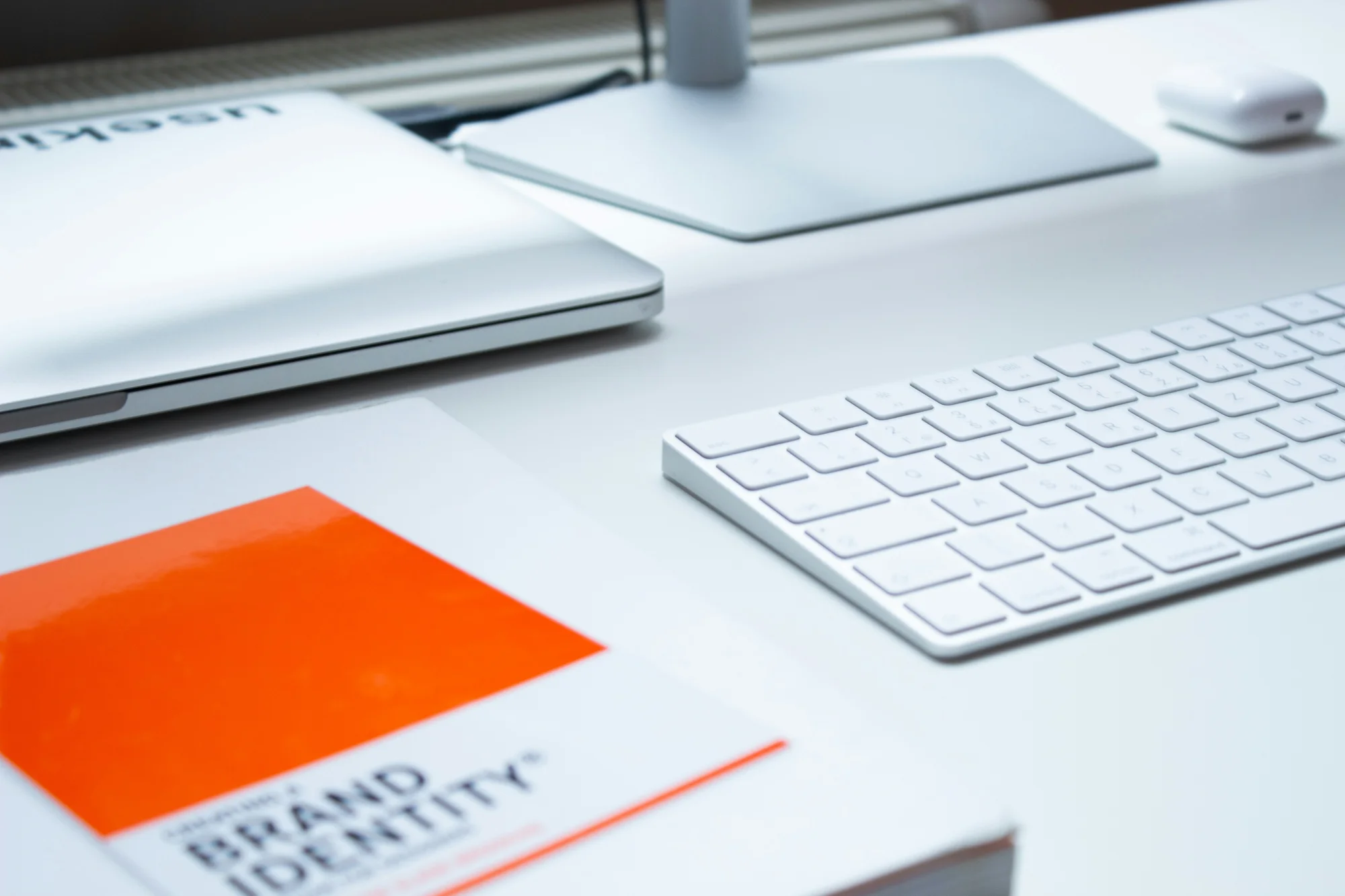 A brand identity book beside a keyboard and laptop on a design workspace.